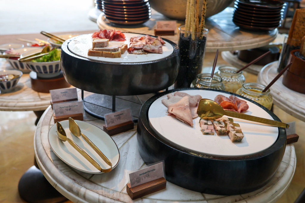 تشكيلة اللحوم الباردة في الإفطار: بارما هام، وباتيه لحم الخنزير داخل عجين pâté en croûte، وجامبون بيرسييه بقطع لحم وبقدونس واضحة.