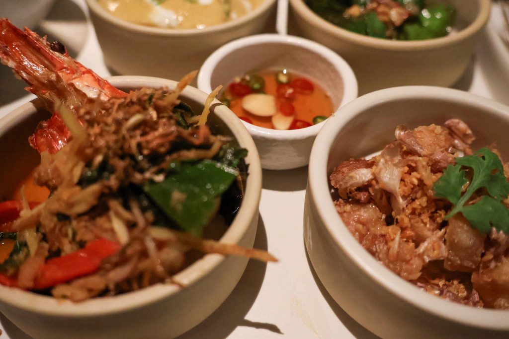 يسارًا Goong Phad Prik Grachai، روبيان مشوّح بالنباتات العطرية والفلفل؛ ويمينًا Moo Sam Chan Thod Kratiam، لحم خنزير مقلي بالثوم والكزبرة.