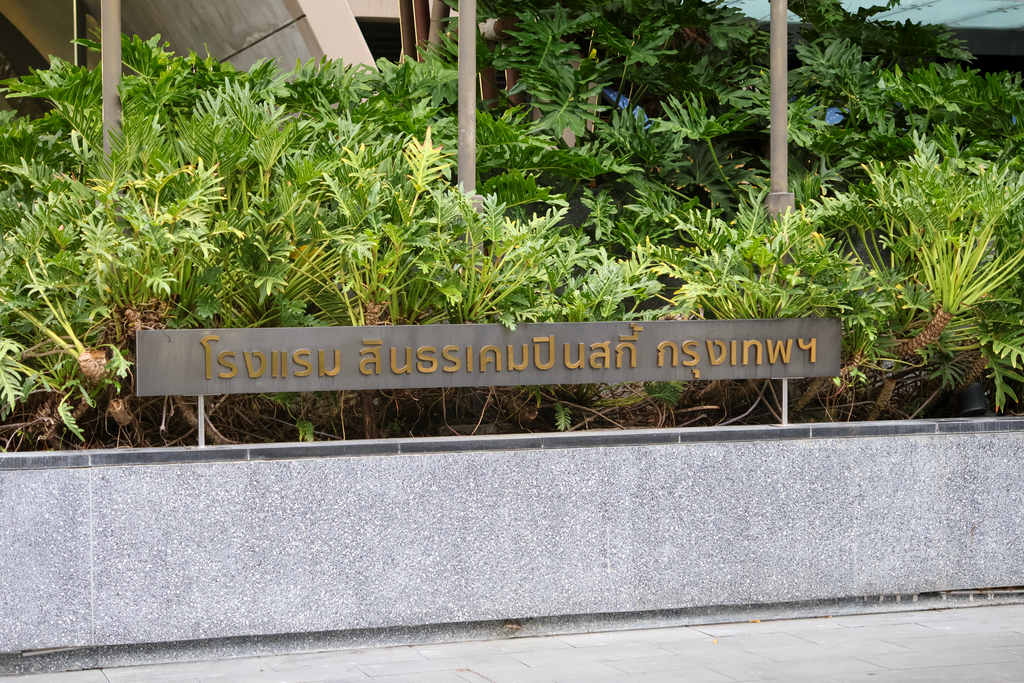 ชื่อโรงแรมภาษาไทยบนฐานสีเทาด้านหน้าพุ่มไม้