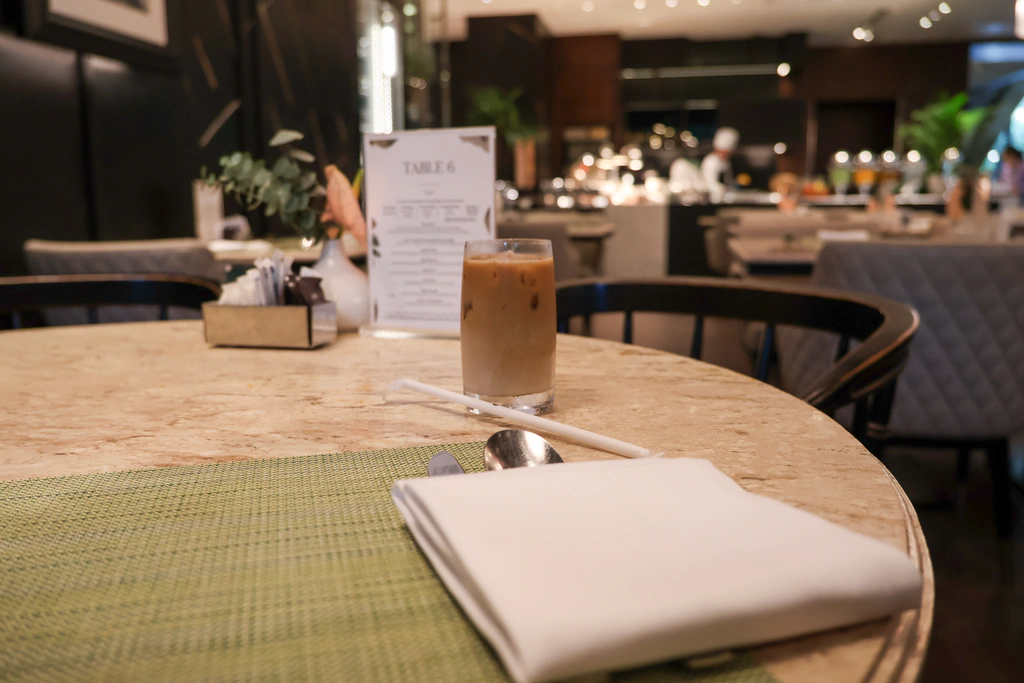 กาแฟเย็นในแก้วหลังแผ่นรองเขียวกับผ้าเช็ดปากขาว