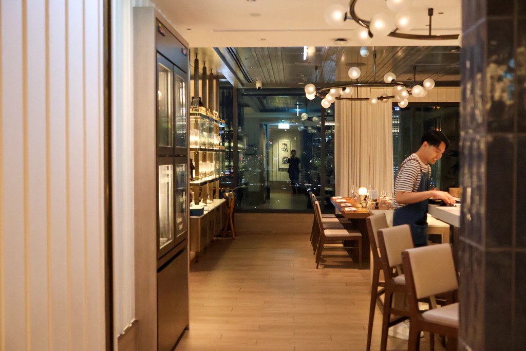 ทางเข้า Bistrot De La Mer ตามผนังสีอ่อนกับพื้นไม้ไปสู่ที่นั่งริมหน้าต่าง