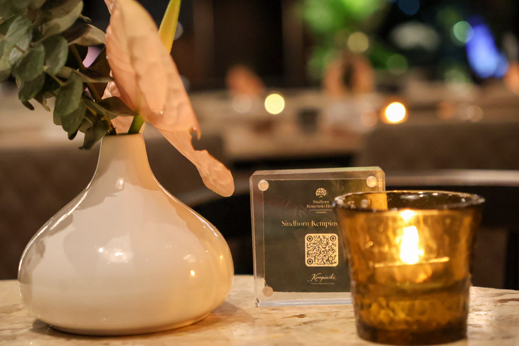 แจกันขาวข้างป้าย QR และเชิงเทียนแก้วโทนทอง