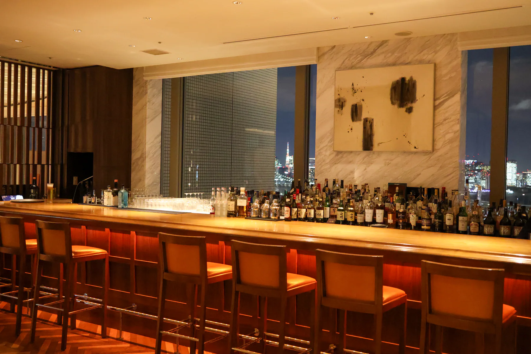 منضدة خشبية طويلة ومقاعد مرتفعة وجدار رخامي في The Bar & Lounge